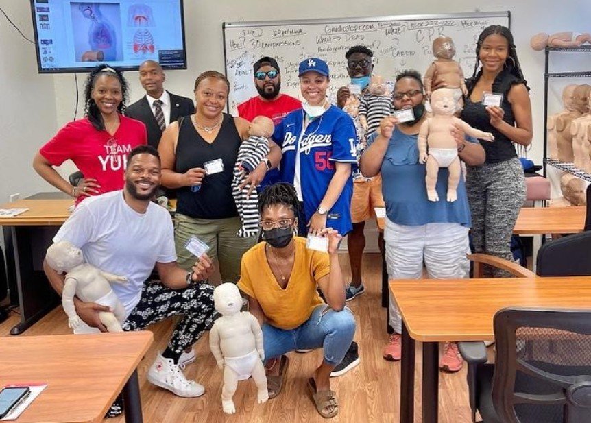 CPR class graduates holding certification cards and training manikins in the classroom